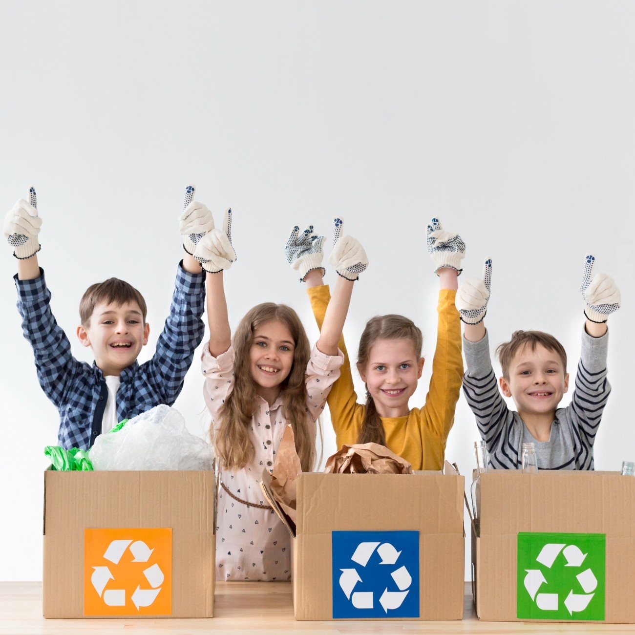 Two smiling girls holding cardboard recycling boxes standing next to a whiteboard with a colored recycling symbol and words glass, plastic, and paper.