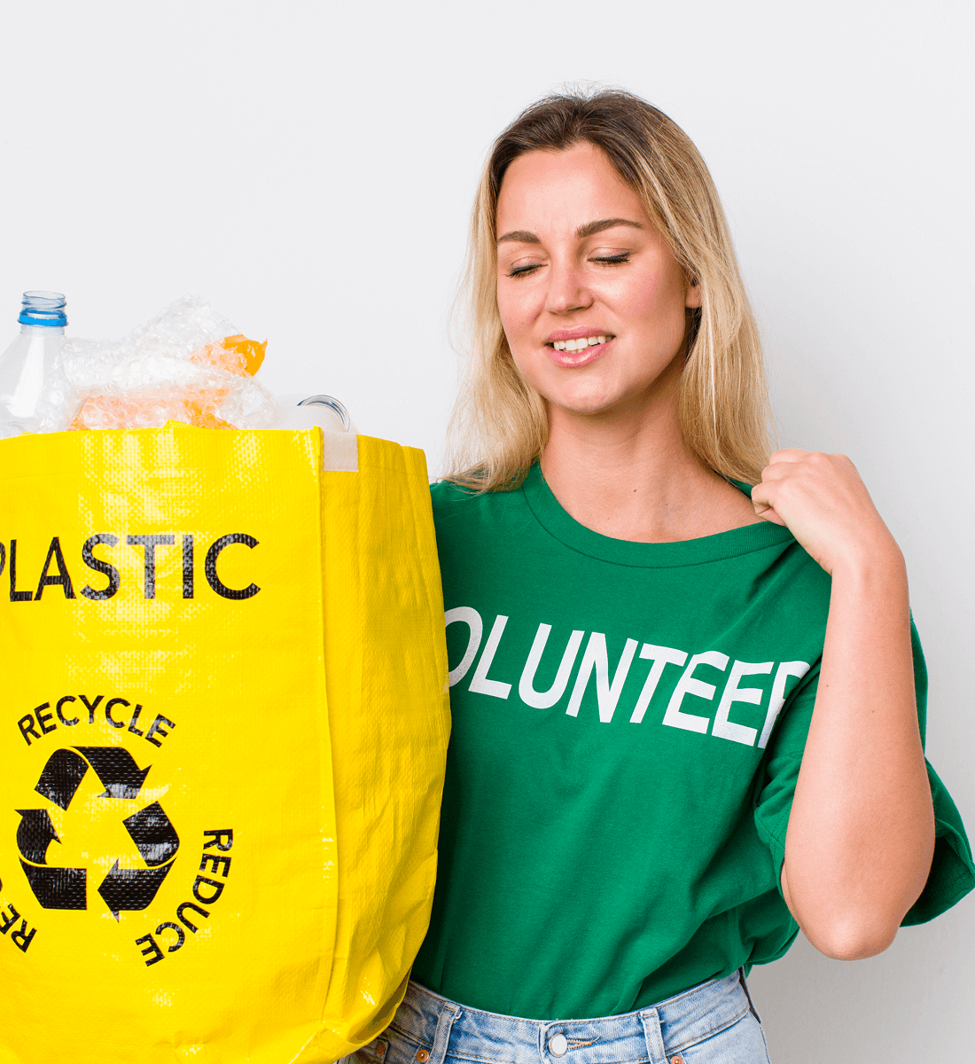 Woman wearing a green volunteer shirt holding a yellow recycling bag filled with plastic waste.