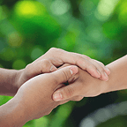 Two people holding hands gently against a blurred green natural background.
