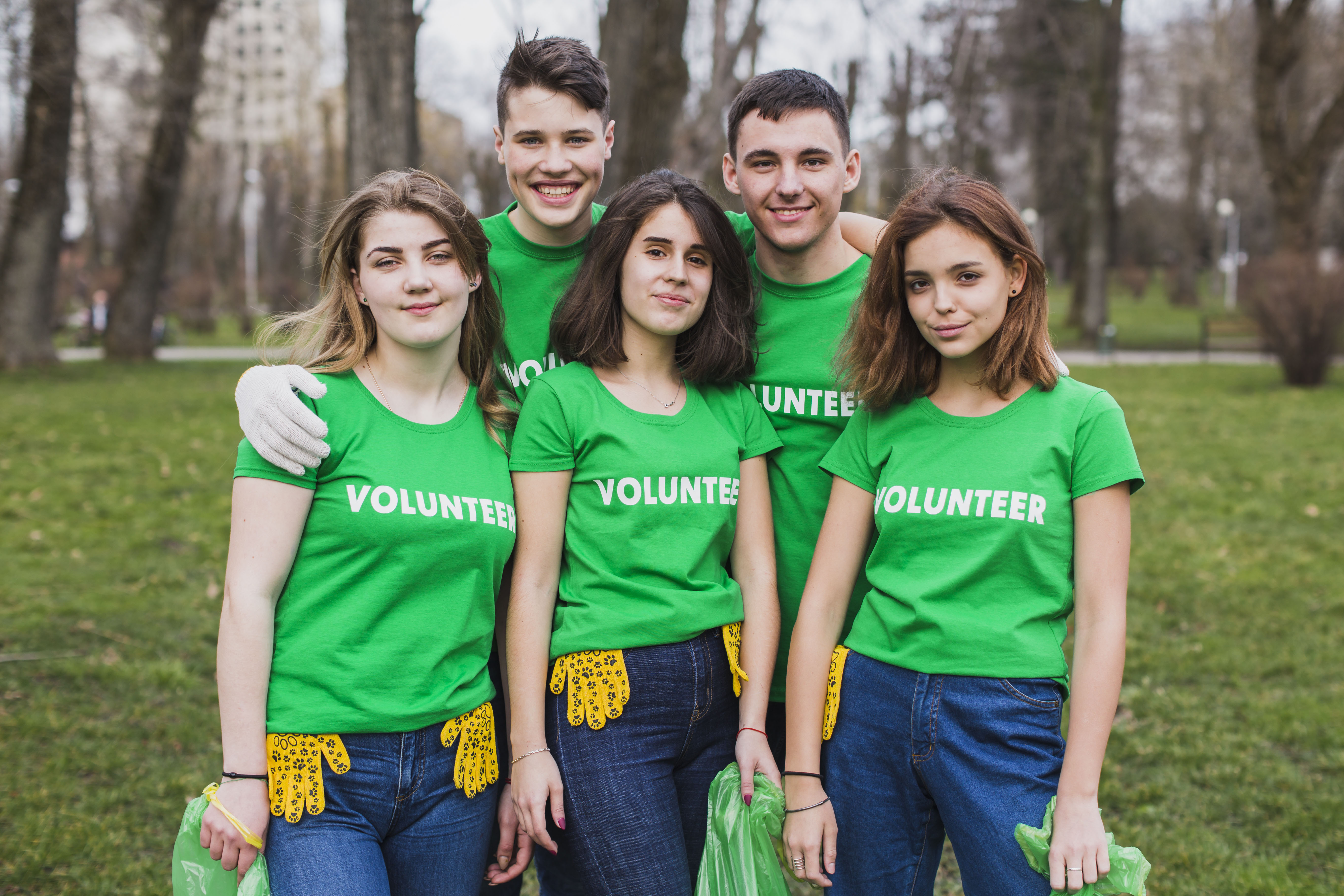 Group of five young volunteers wearing matching T-shirts and holding plastic bags and gloves.