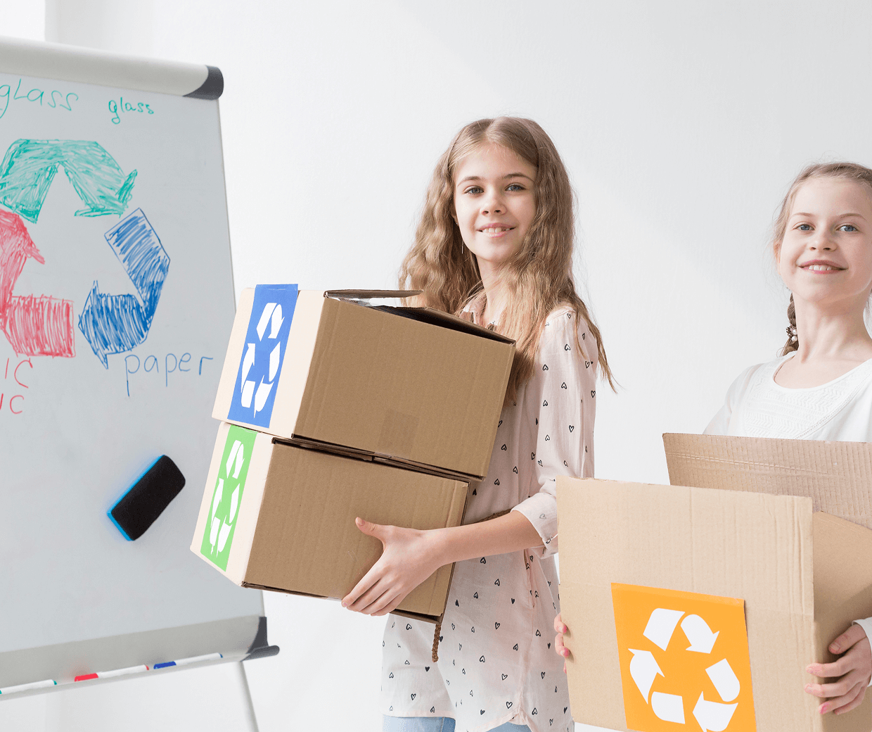 Two women wearing green recycling t-shirts holding a wooden crate filled with recyclable cans and containers.