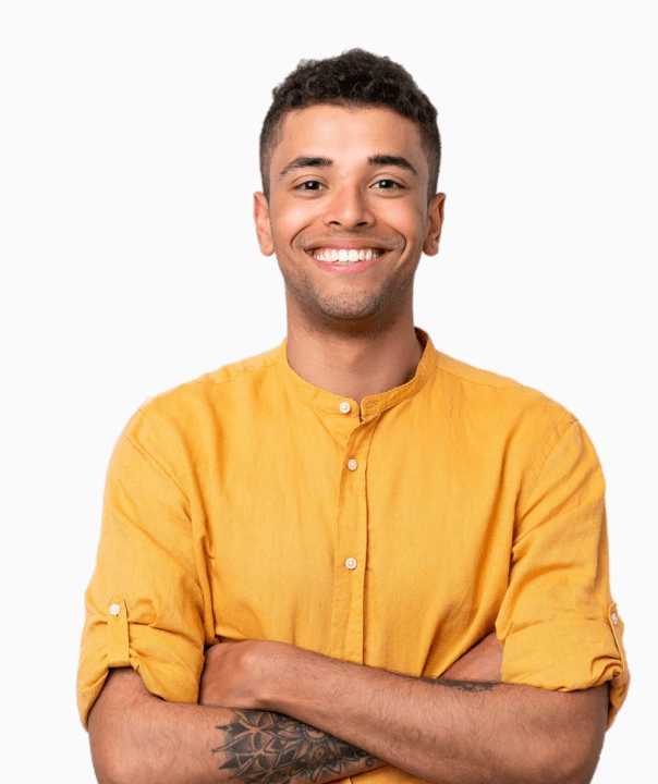 Smiling young man with short curly hair wearing a yellow shirt with rolled-up sleeves and a tattoo on his forearm, standing with arms crossed.