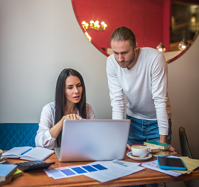Two coworkers discussing work while looking at a laptop in a modern office with documents and coffee on the table.