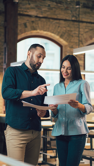 Man and woman reviewing documents together in a modern office with exposed brick walls and arched windows.