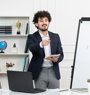 Man in business attire standing and pointing with a pen while holding a notebook in an office setting.