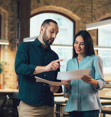 Two colleagues reviewing documents together in an office, one pointing at the papers while the other smiles.