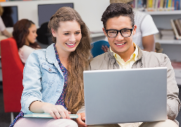 Smiling young man and woman looking at a laptop screen together in a library setting.